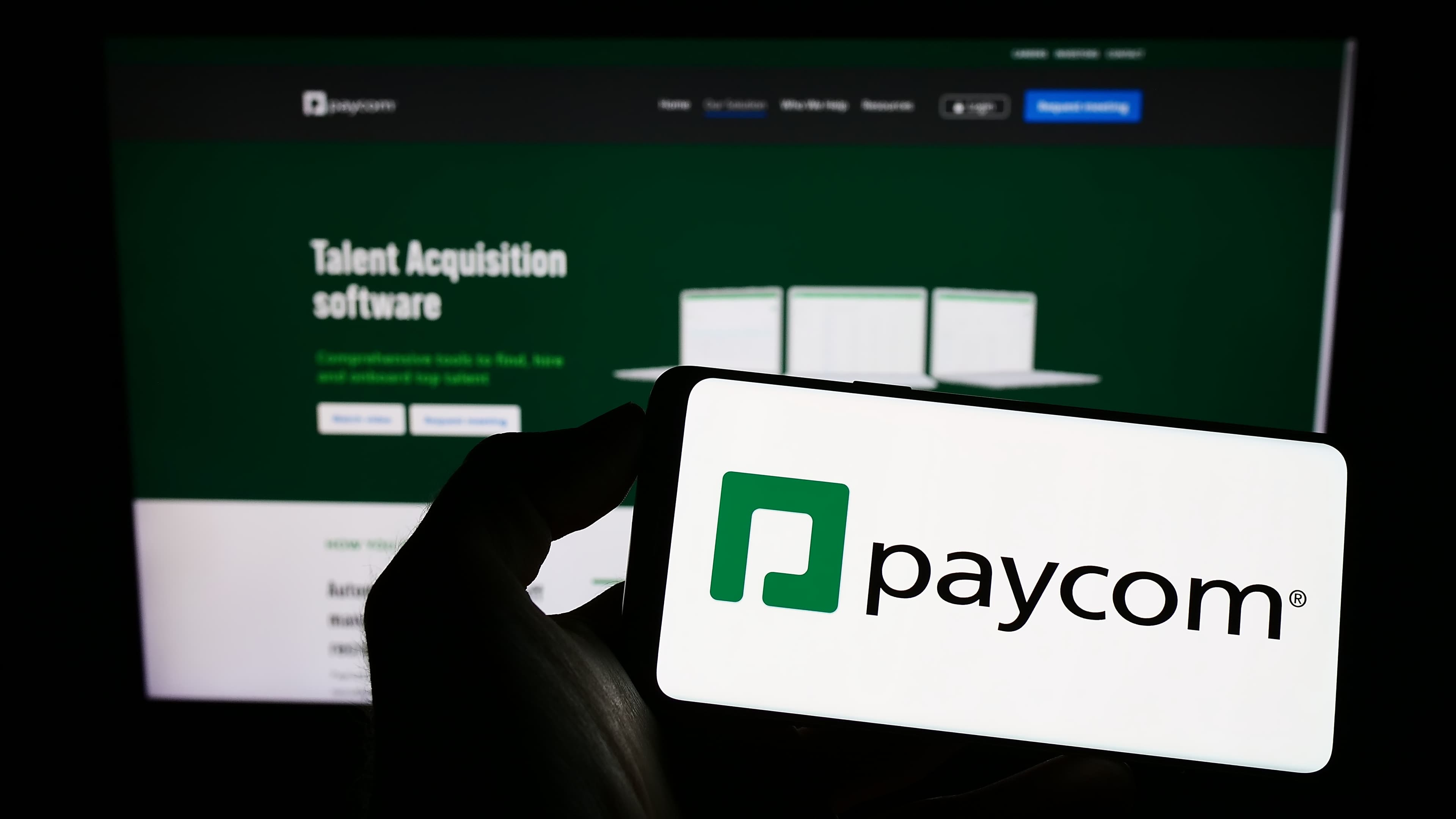 A phone showing the Paycom logo in front of Paycom’s public talent-acquisition page